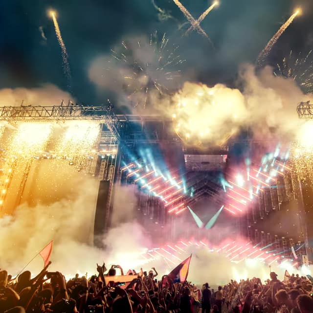 A festival crowd facing a lit stage as fireworks burst overhead